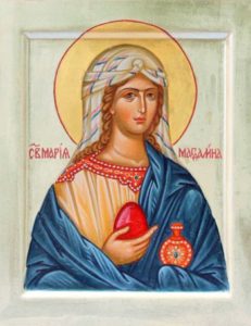 Beautiful icon of Mary Magdalen. She is wearing a blue robe around a yellow-gold top that has beautiful red embroidery at the top. She is holding a large red Easter Egg in her right hand, and carrying a decorated red vessel (about the same size as the large egg), presumably containing myrrh. Her hair is in gold braids that come down past her shoulders, and are partially visible underneath her white headdress with blue and white stripes.